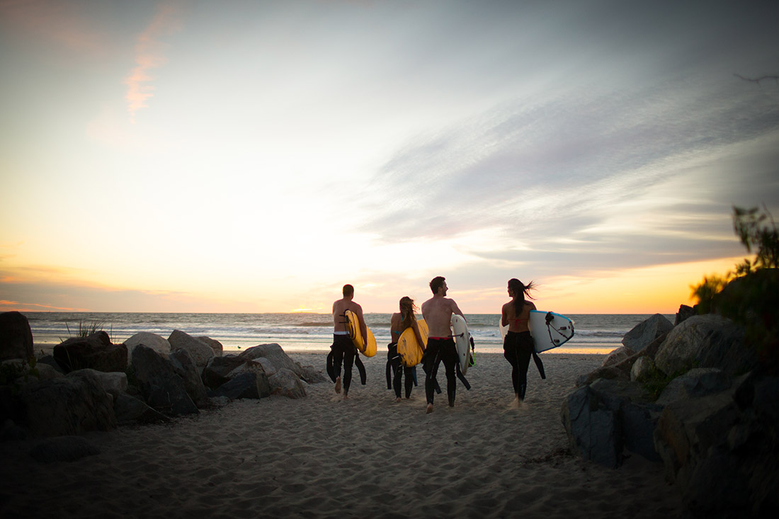 a group of friends carrying surfboards towards the ocean