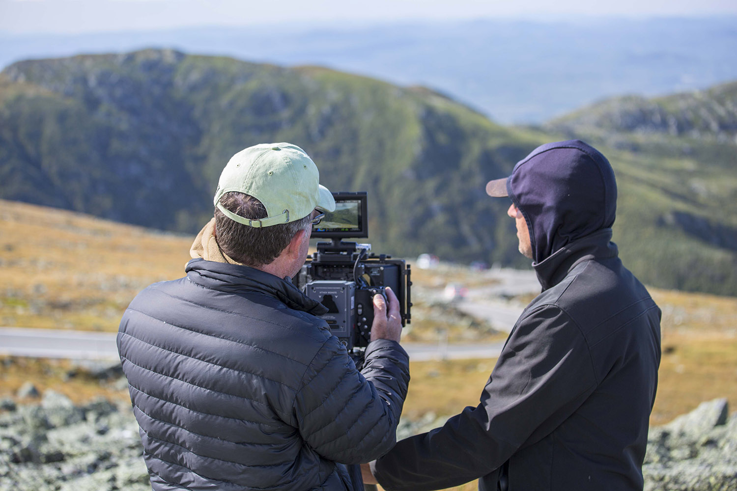 two men with a camera on a mountain by a winding road