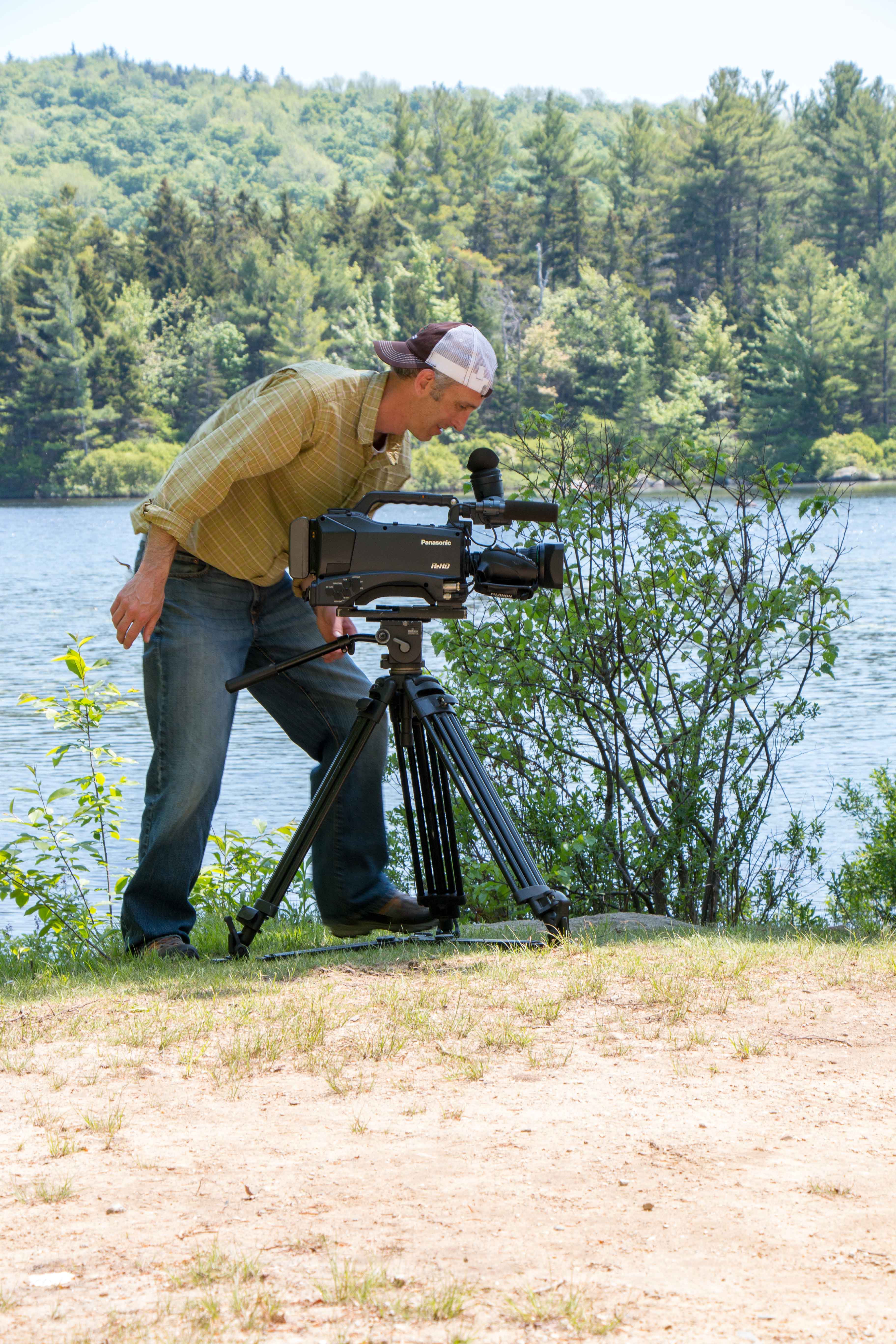 a man with a camera on a tripod by a lake