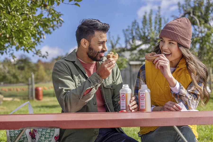 a man and woman eating donuts at a picnic table in fall