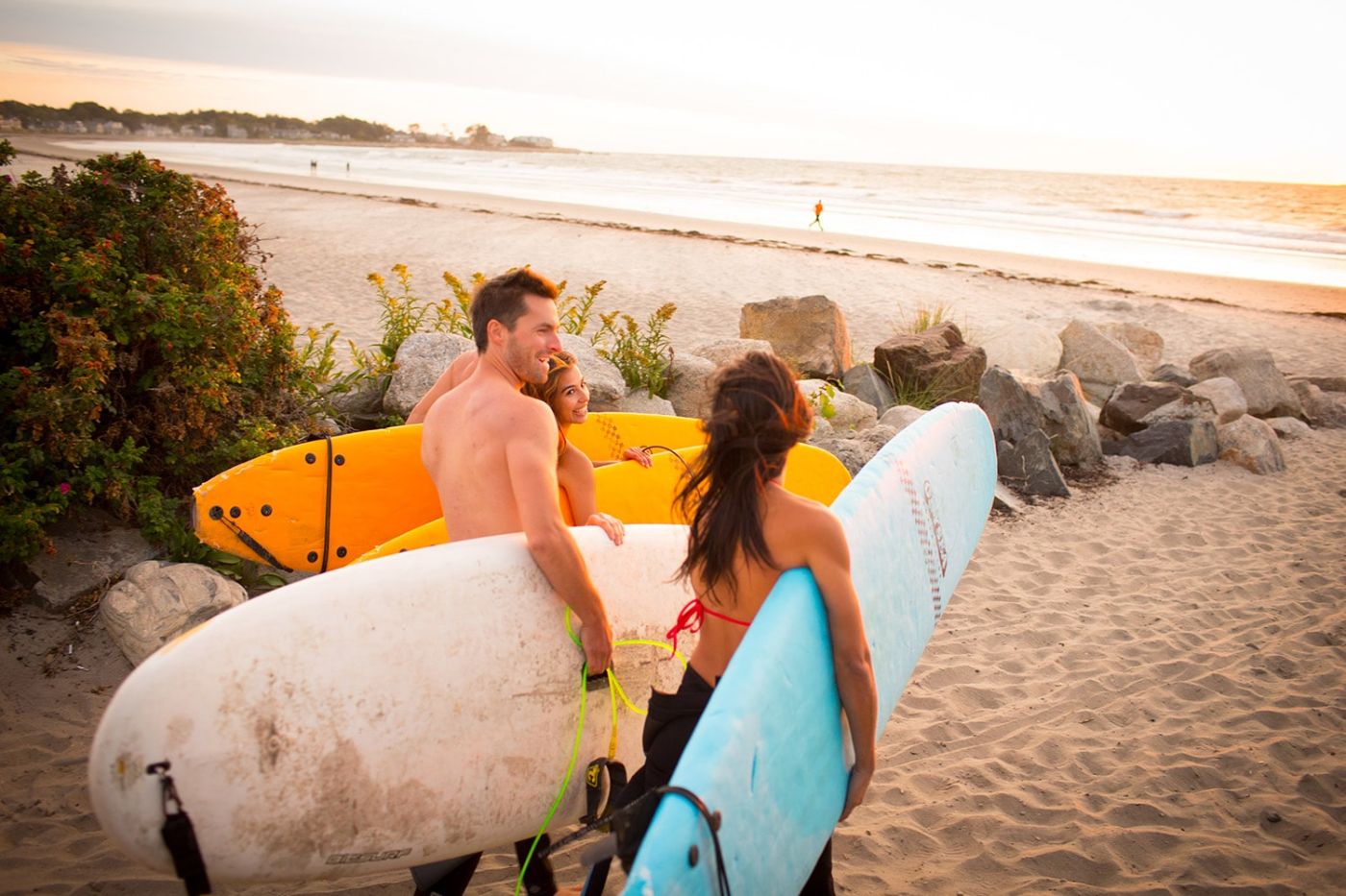 3 surfers walking towards the ocean with their surf boards smiling