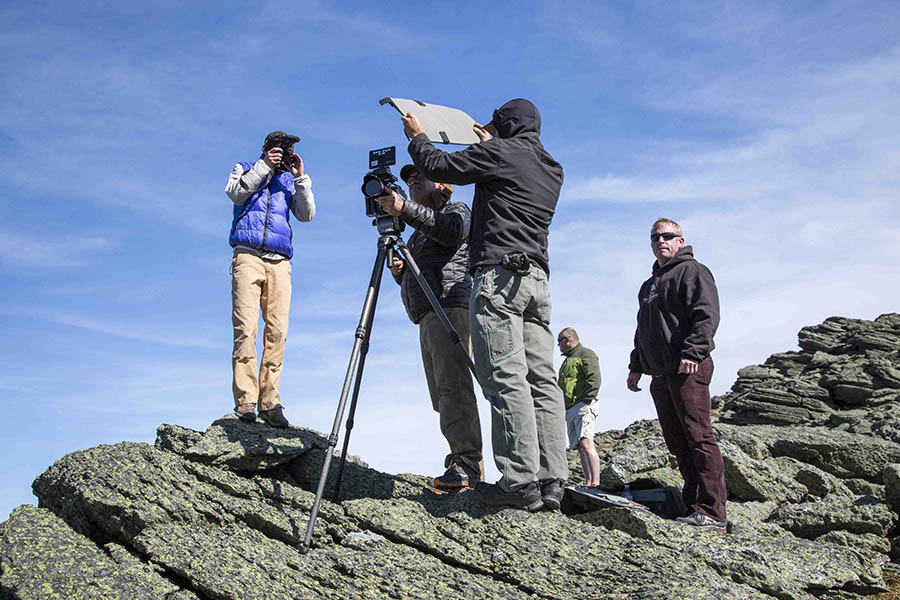 5 men standing on a rock with a video camera