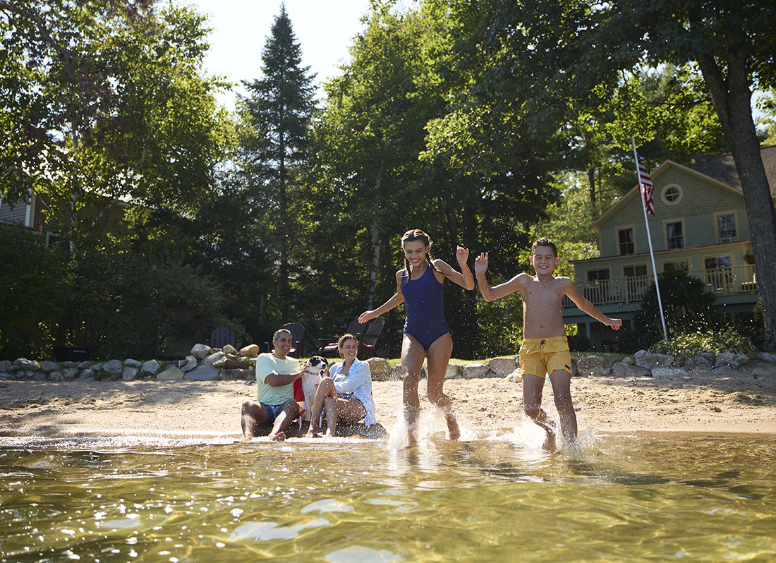 two kids running into a lake with their parents and dog sitting on shore behind them