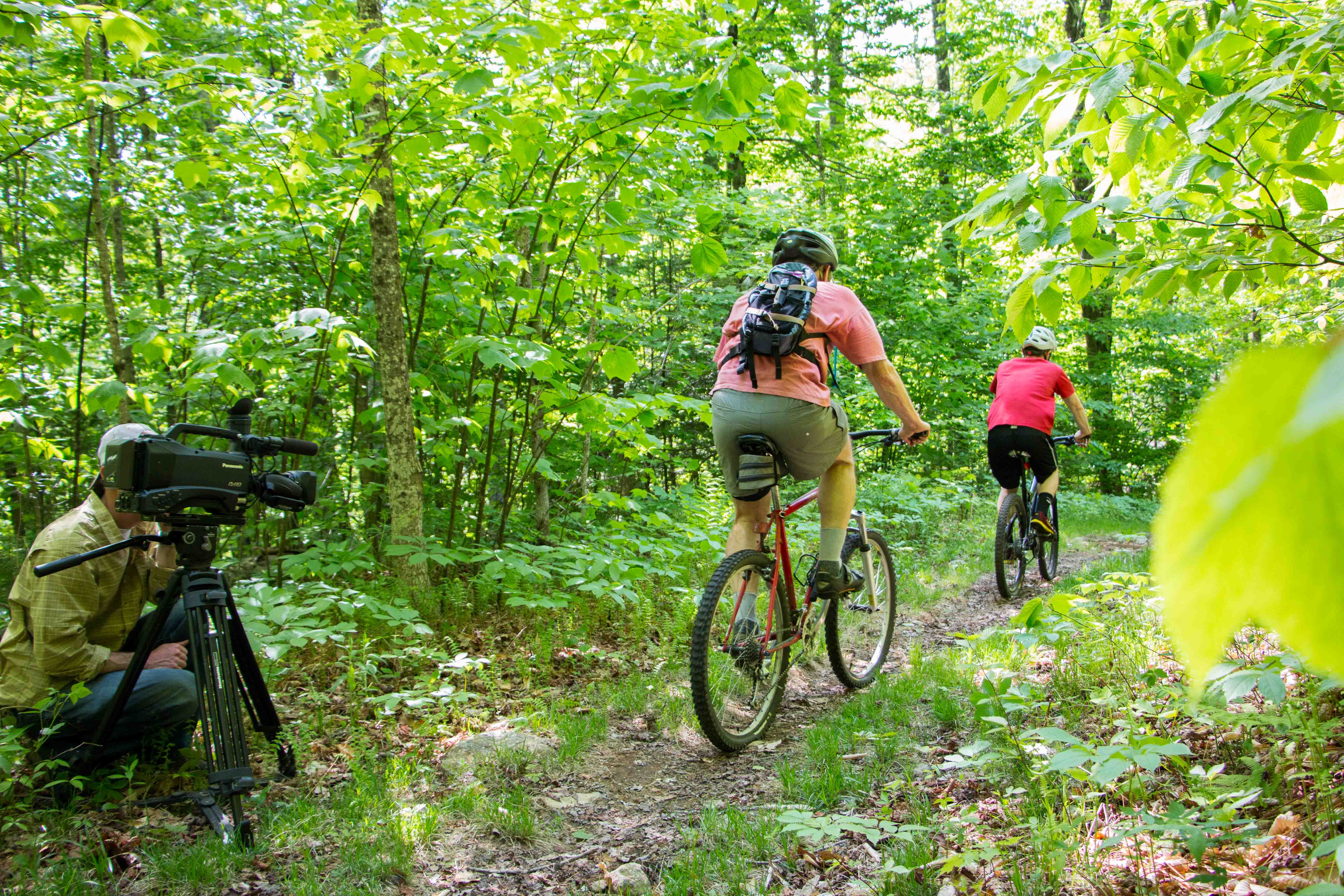 a man filming two people riding bikes in the woods