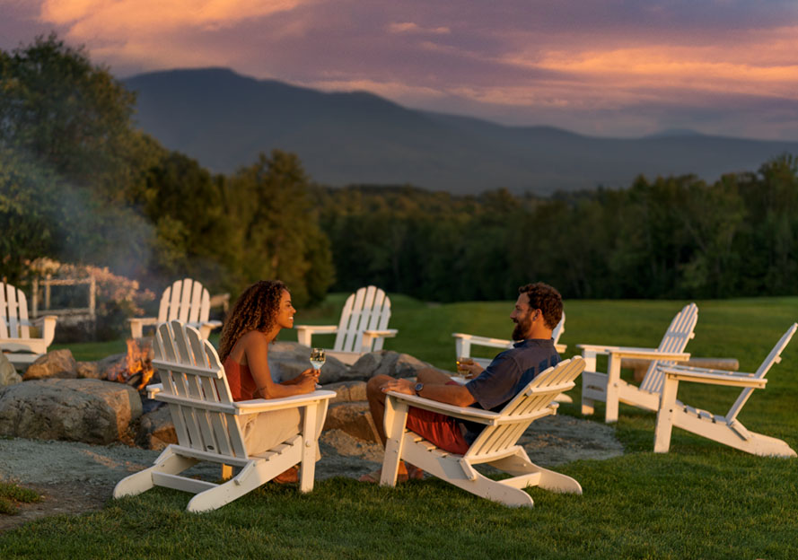 a man and woman by a firepit at sunset