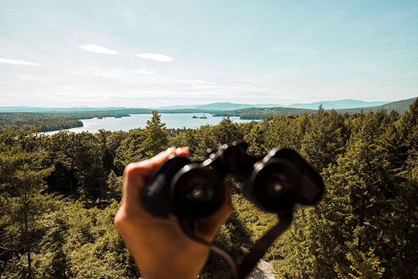 a hand holding binoculars across a lake