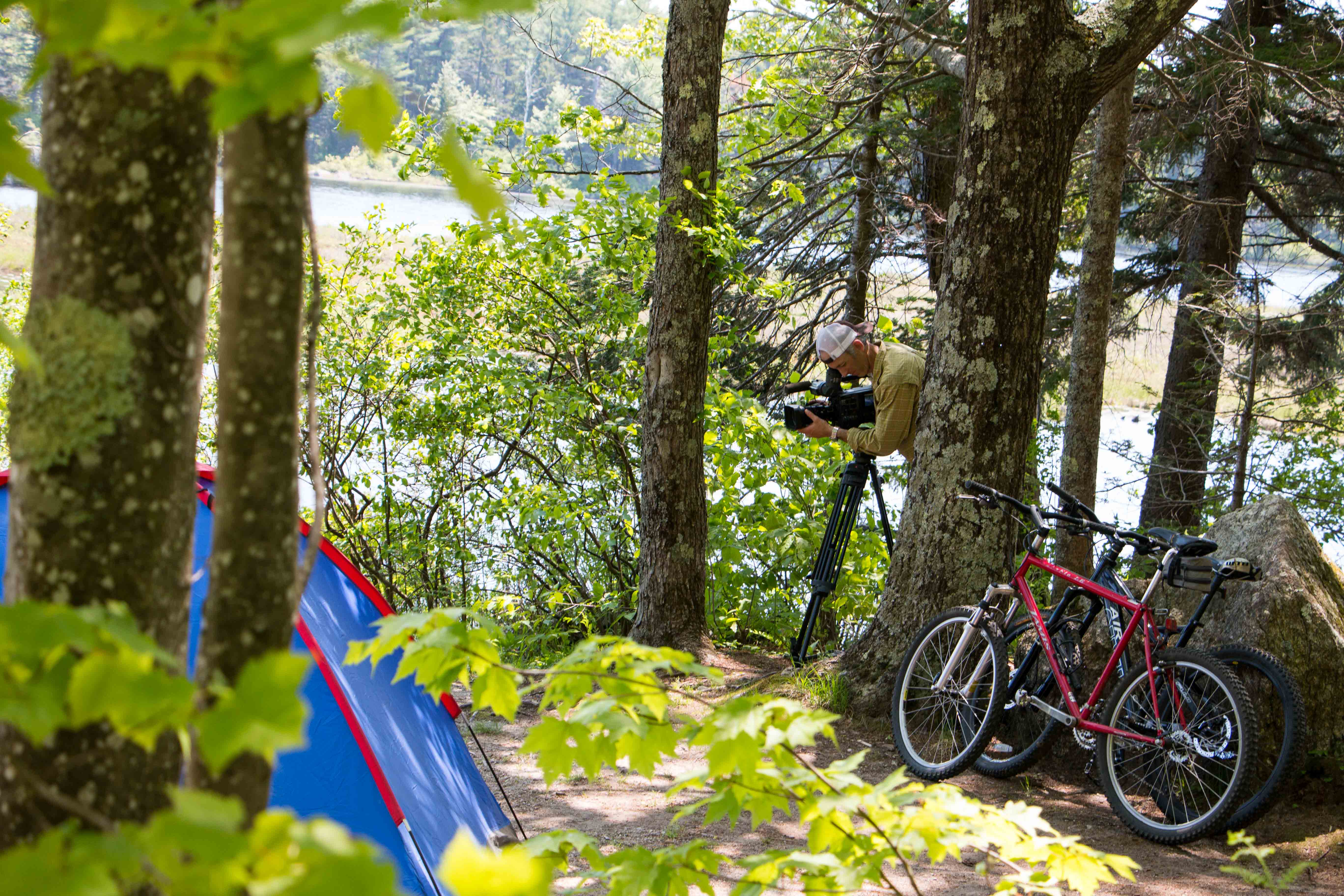 a man with a camera in the woods near a bicycle and tent