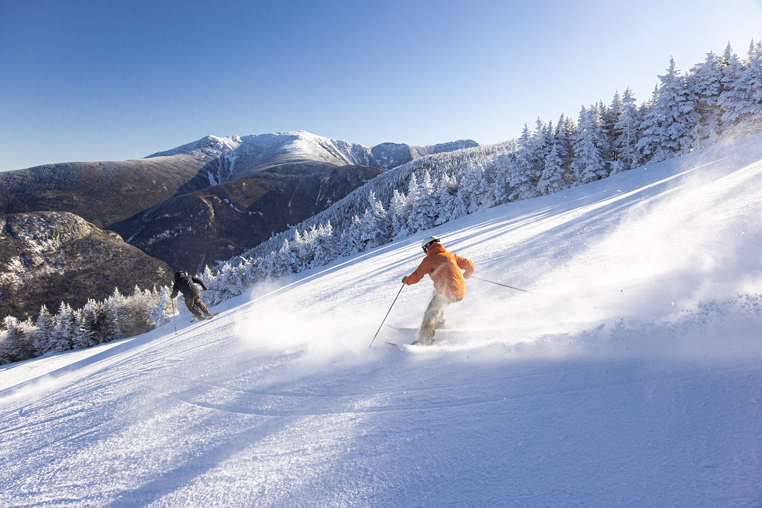 two people skiing down a trail with snow covered mountains in the background