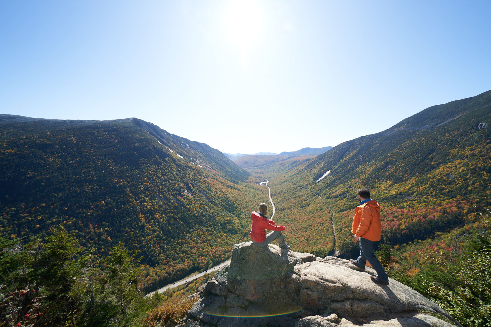 2 people sitting at an overlook on a mountain