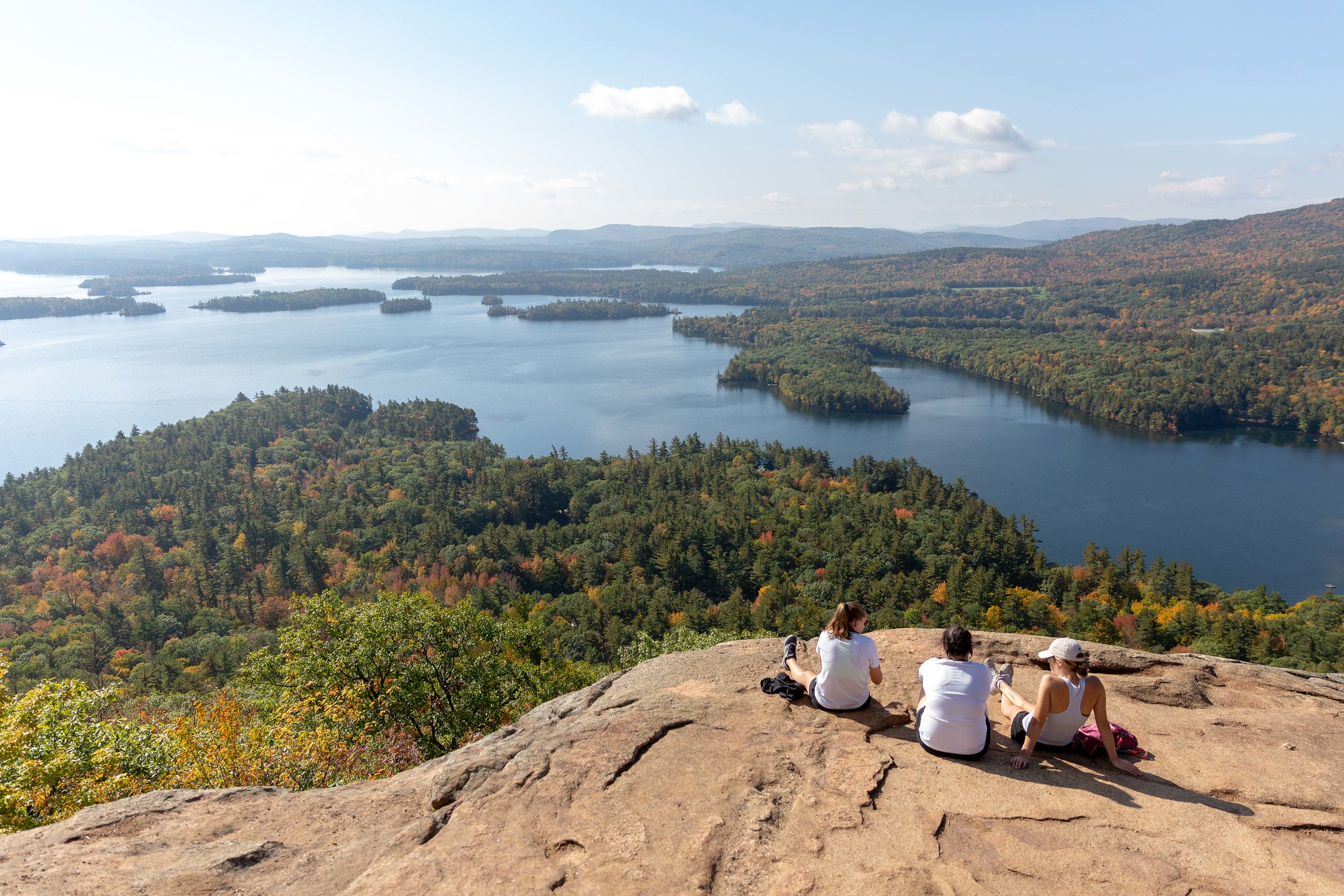 Hikers sitting on a mountain peak overlooking a forest and lake