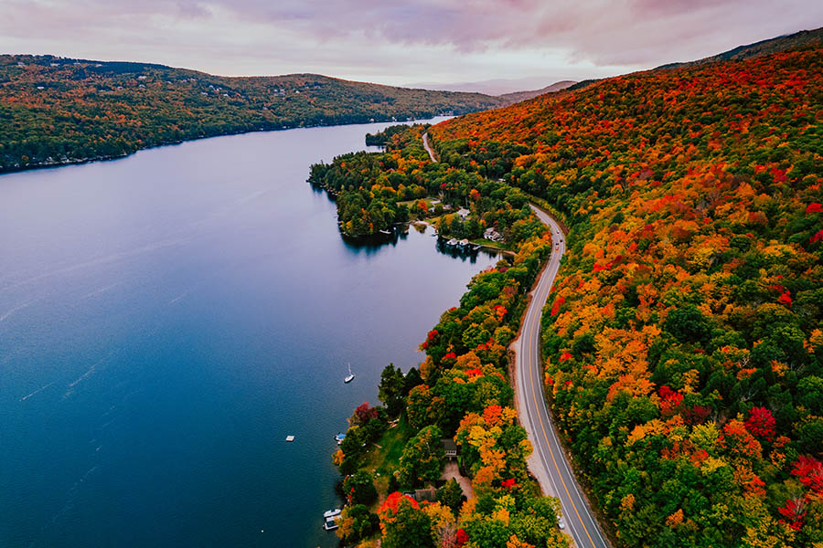 An aerial view of fall foliage and a road next to a lake